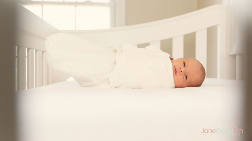 newborn in crib in white swaddle
