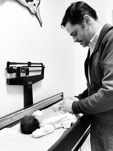 black and white iphone photo of newborn on weighing table with dad